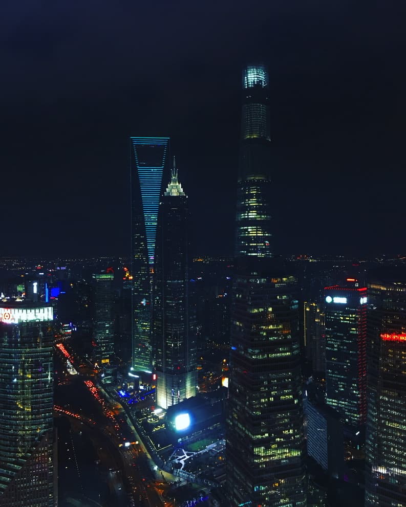 A city skyline of illuminated skyscrapers at night, including a distinctive twisting tower and a trapezoid-shaped building